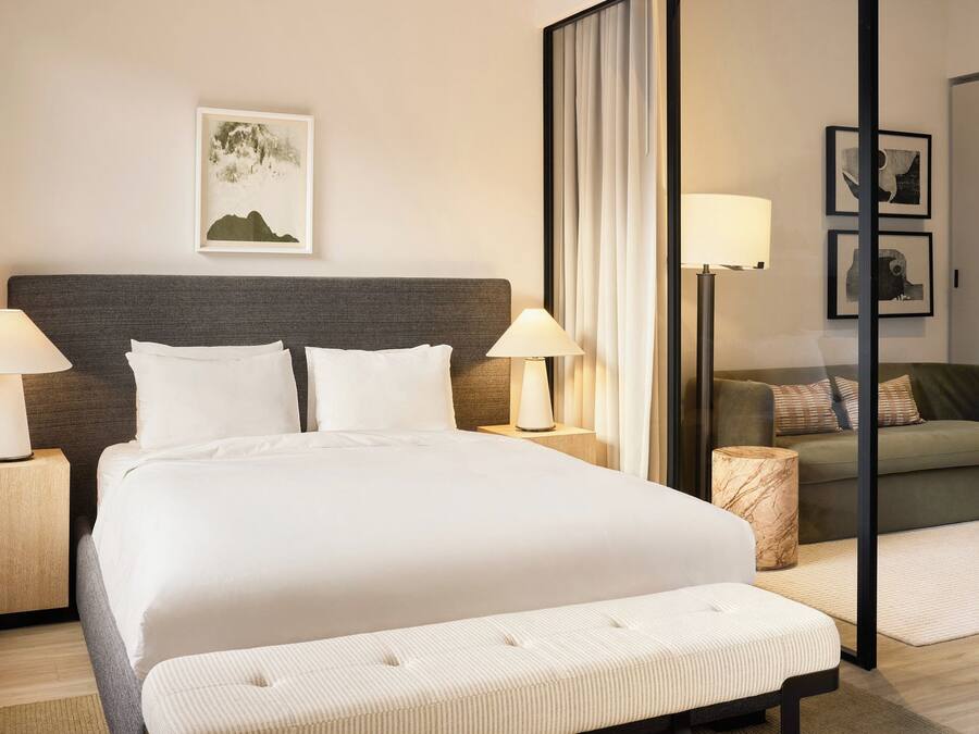 Una habitación de hotel con una cama grande, dos lámparas de noche, un sofá, una mesita y un cuadro en la pared.
