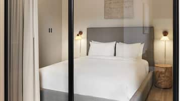 Un dormitorio moderno con una cama grande, dos lámparas de noche, una mesita de madera pequeña y una obra de arte colgada en la pared.