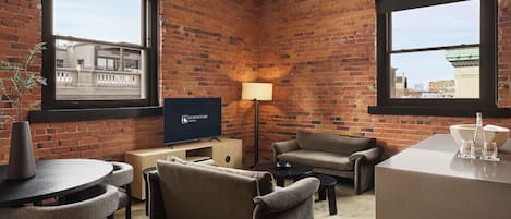 A hotel room with brick walls, a flat-screen TV, a sofa, a small table, and a lamp.