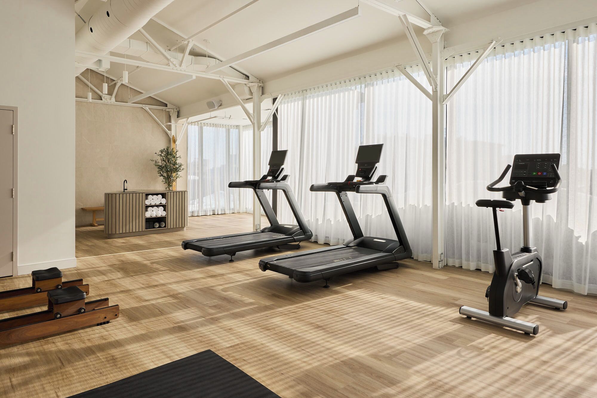 A gym with treadmills, a wooden floor, and a large window with sheer curtains.