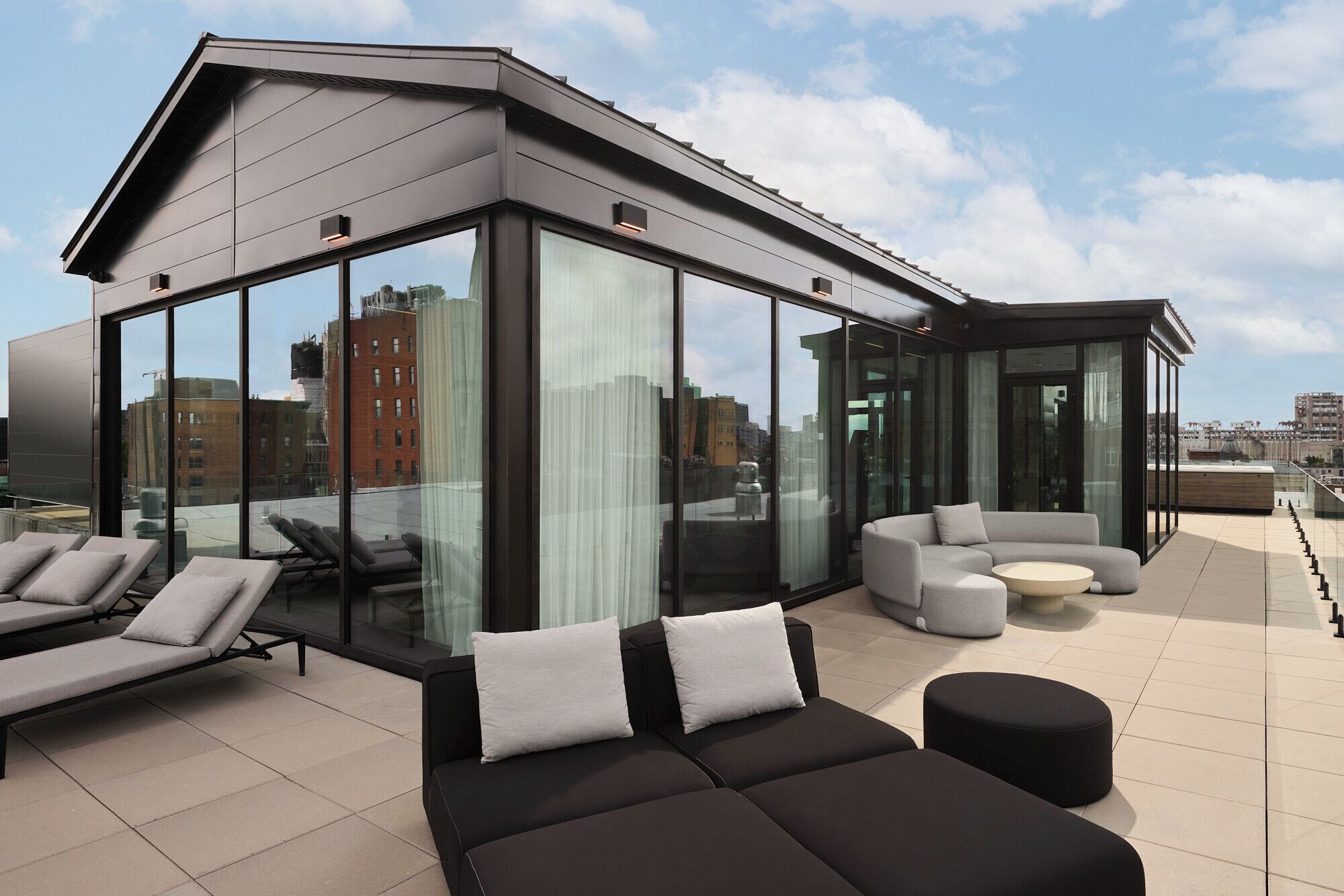 Una terraza moderna en la azotea con cerramiento de vidrio curvo, mobiliario exterior y vistas a la ciudad.