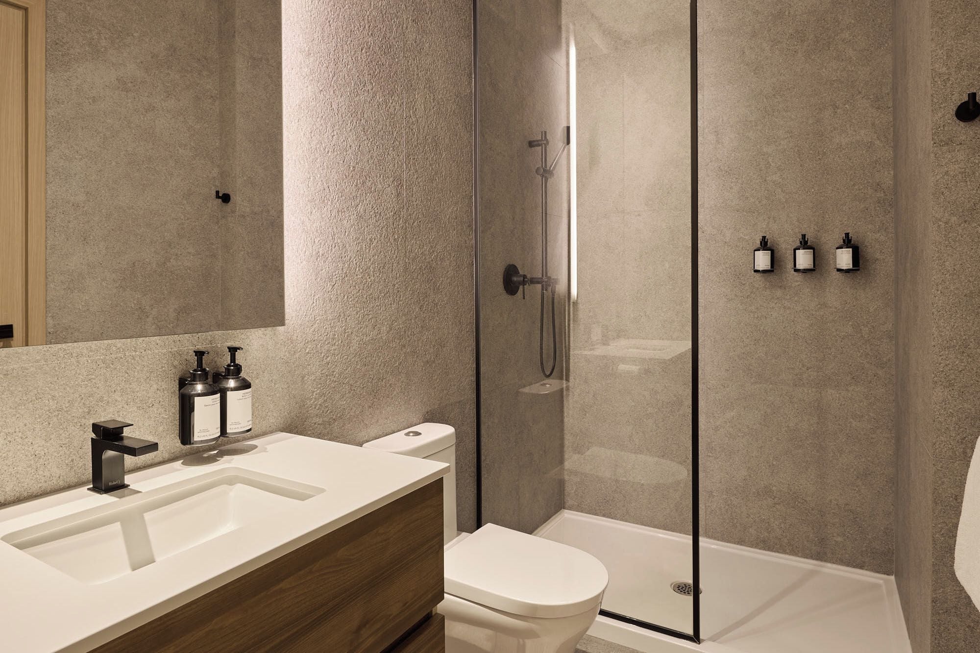 Une salle de bain moderne avec une douche à parois de verre, un lavabo blanc avec un meuble-vasque en bois et des toilettes.