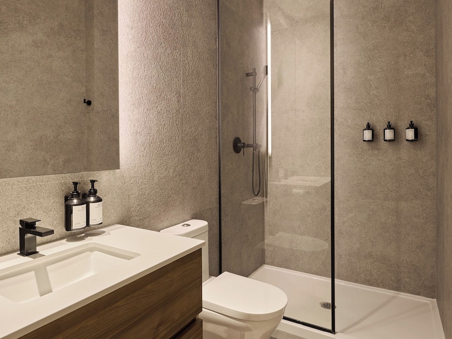 A modern bathroom with a glass-enclosed shower, a white sink with a wooden vanity, and a toilet.