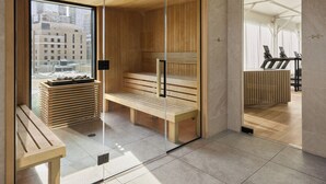 Una sauna con bancos de madera, puerta de cristal y vistas a la ciudad a través de amplios ventanales.
