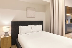 Habitación de hotel moderna con cama, lámpara de noche, una obra de arte en la pared y vistas al área de la cocina.