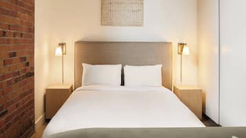 Habitación de hotel con pared de ladrillo, una cama grande con ropa blanca, dos mesitas de noche con lámparas y una obra de arte colgada en la pared.