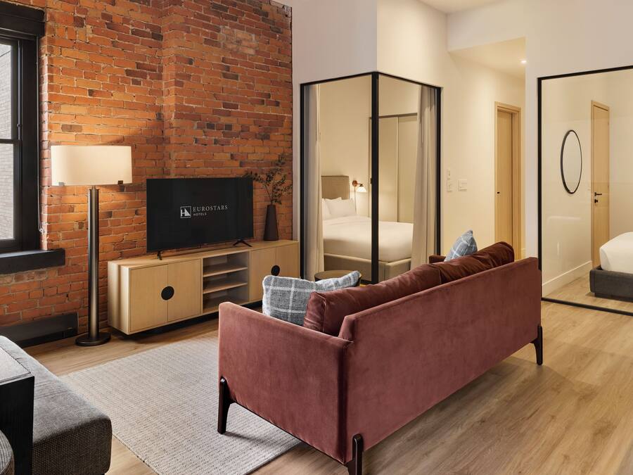 Ett modernt hotellrum med en tegelvägg, en platt-TV, en soffa, en säng och en spegel.