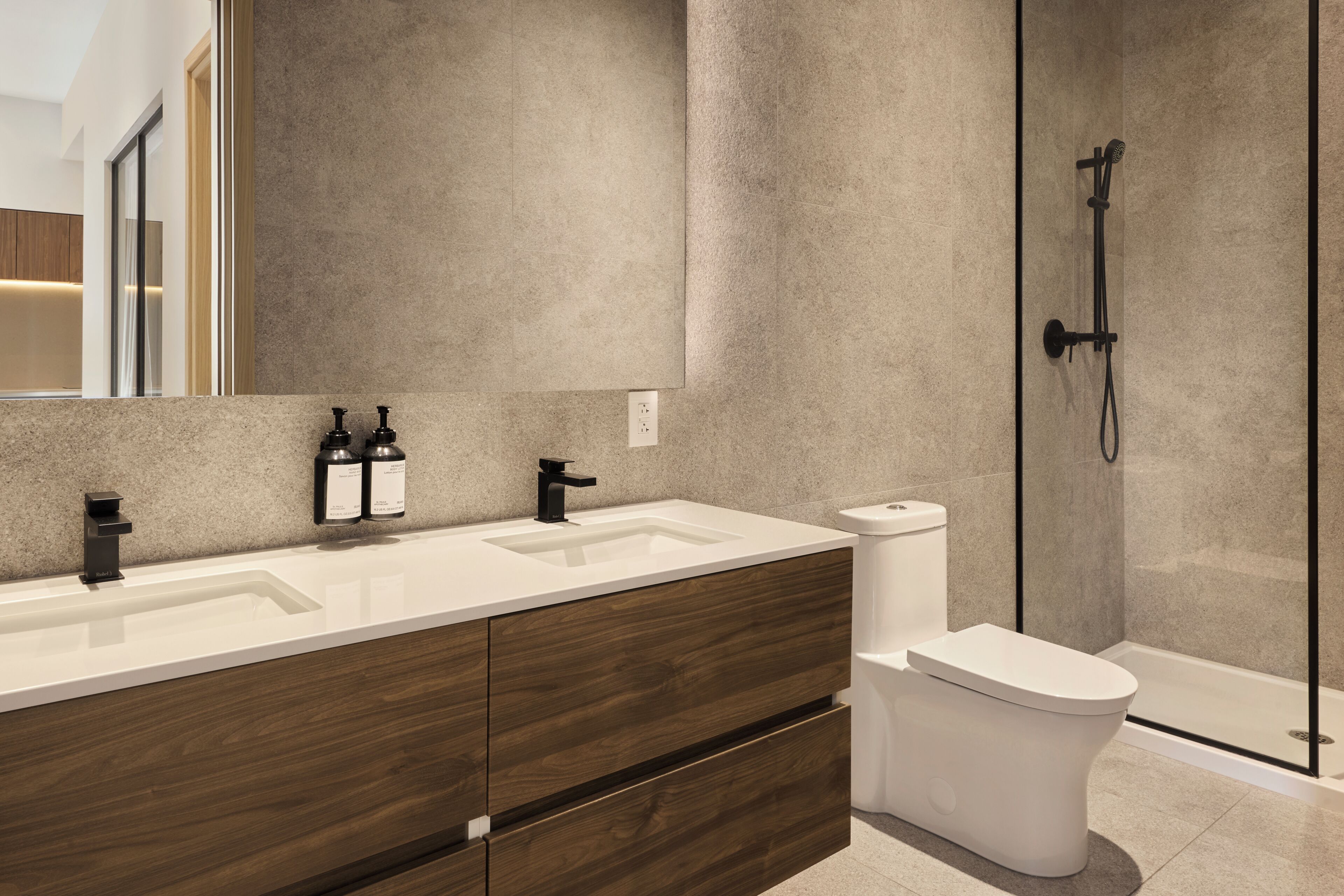 A modern bathroom with a double sink vanity, a toilet, and a glass-enclosed shower.