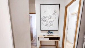 Un pasillo con un escritorio de madera, una obra de arte enmarcada con rosas y mariposas, y una puerta con marco de madera.