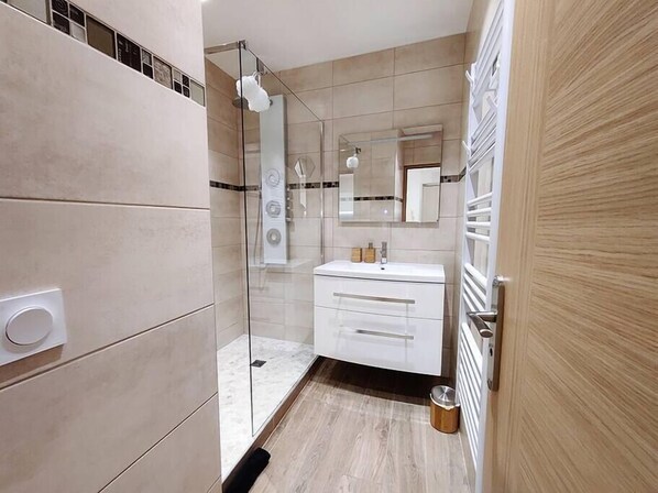 A modern bathroom with a glass shower enclosure, a white vanity, and a wooden door.