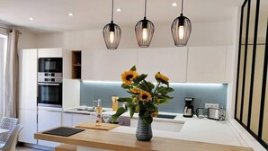 Una cocina moderna con una isla central, lámparas colgantes y un jarrón con girasoles.