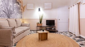 A living room with a beige sofa, a round woven rug, a small wooden table, a television, and a wall-mounted light. - Unique studio, Old Town Nice, 2min from the beach,AC (Nice)