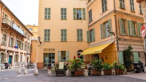 A street with a yellow awning cafe, outdoor seating, and a building with green shutters. - Unique studio, Old Town Nice, 2min from the beach,AC (Nice)