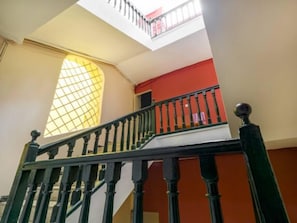 Uma escadaria com balaústres pretos, uma parede vermelha e uma janela com padrão de grade.