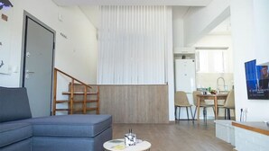 Un salon moderne avec un canapé gris, une petite table ronde et un escalier menant à l’étage supérieur.