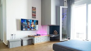 Un salon moderne doté d’un téléviseur à écran plat fixé au mur, d’un néon, d’une cheminée et d’une grande fenêtre.