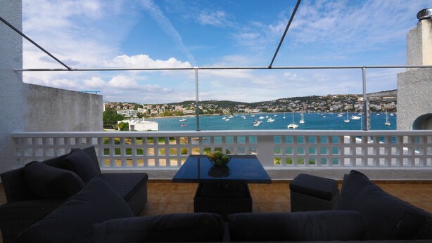 Un balcon agrémenté de meubles en osier, une table avec un vase, et une vue sur les bateaux qui naviguent.