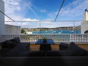 Un balcón con muebles de mimbre, una mesa con un jarrón y vistas a barcos en el agua.