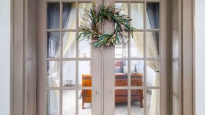 A door with a wreath and curtains, leading to a room with a bed and a nightstand. - The Cedar House (Steubenville)