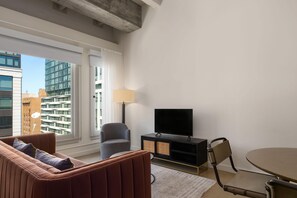 A modern living room with a sofa, armchair, TV, and dining table. - Reside Craftsman Los Angeles, a Wyndham Residence (Los Angeles)