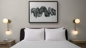 A bedroom with a bed, two bedside tables, a framed abstract painting, and two wall-mounted lamps.