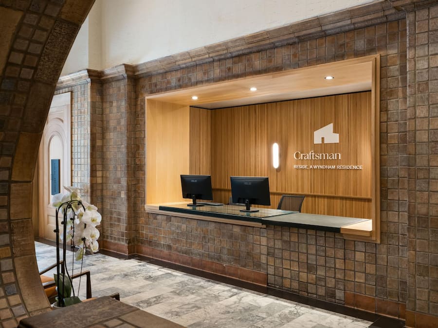 A reception area with a brick wall, two ASUS monitors, and a wooden panel with the Craftsman logo.