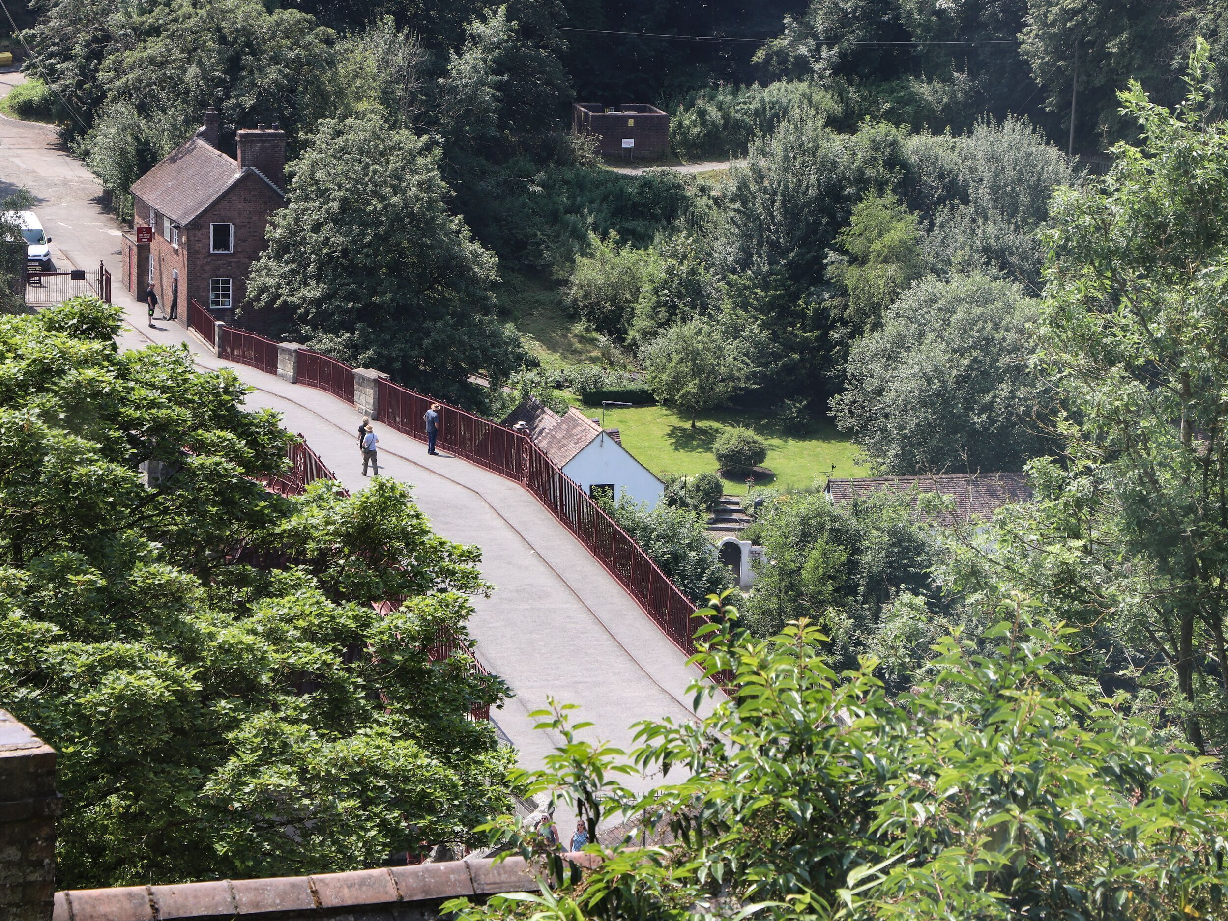 A curved pathway leading to a brick building with a signboard, surrounded by lush greenery and trees.