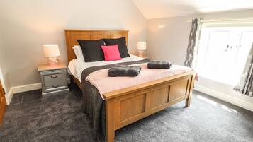 A bedroom with a wooden bed, two bedside tables with lamps, a large window with curtains, and a carpeted floor.