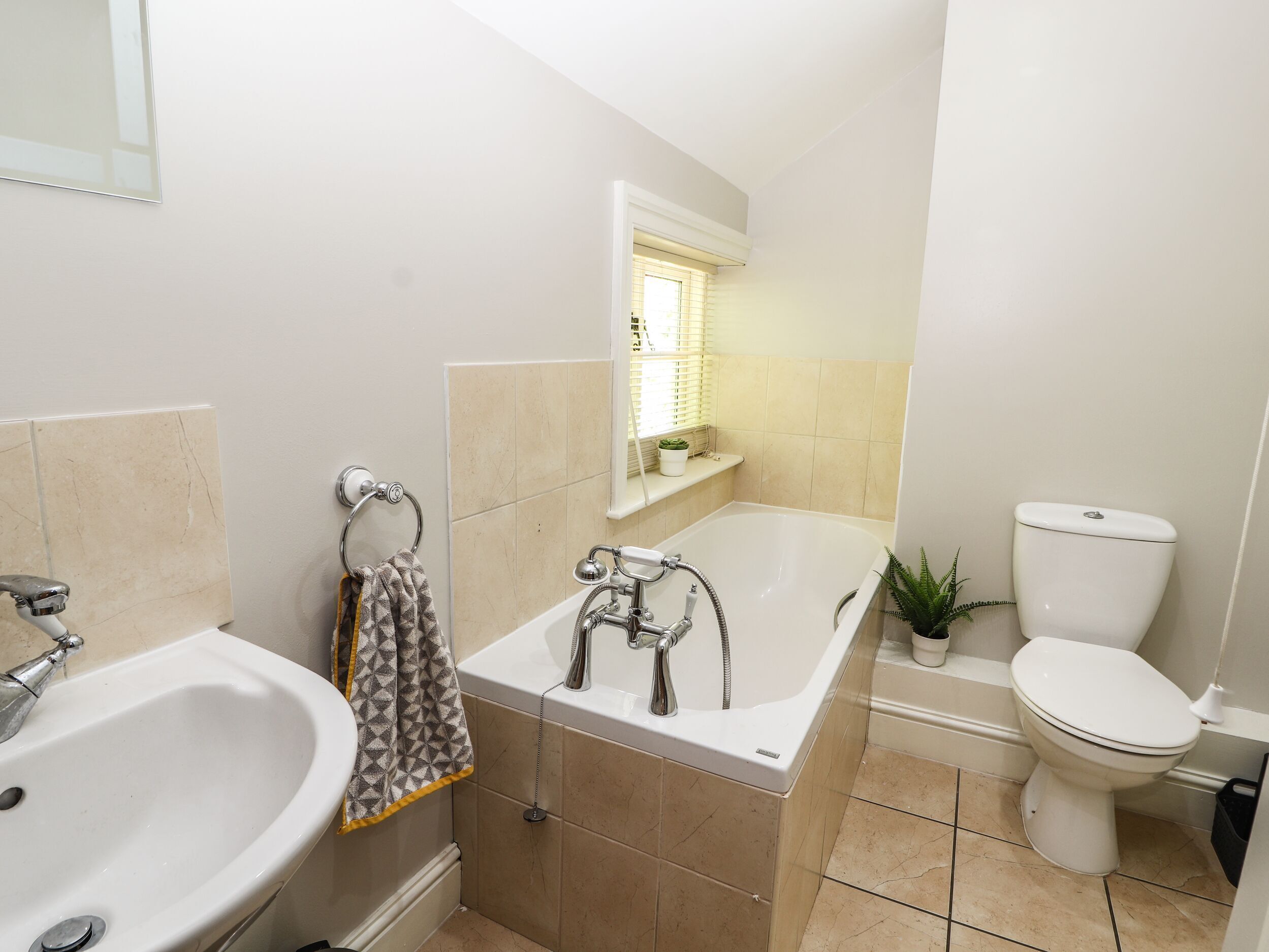 A bathroom with a sink, bathtub, toilet, and a small window with blinds.