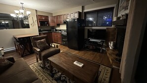 A compact living space with a dining table, sofa, and coffee table. A kitchen area with cabinets and appliances is adjacent. - One bedroom within 2 minute walk to Main Village.
 (Beaverdell)