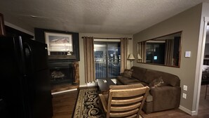 A living room with a fireplace, a sofa, a dining table, and a chair. - One bedroom within 2 minute walk to Main Village.
 (Beaverdell)