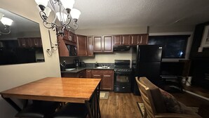 A kitchen with wooden cabinets, a stove, a refrigerator, and a dining area with a table and bar stools. - One bedroom within 2 minute walk to Main Village.
 (Beaverdell)