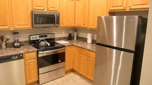 A kitchen with wooden cabinets, stainless steel appliances including a microwave, stove, and refrigerator, and a granite countertop. - Unit D (Moss Point)