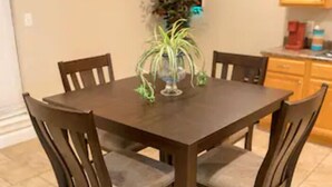 A dining area with a dark wooden table and four chairs, a potted plant, and a clock on the wall. - Unit D (Moss Point)