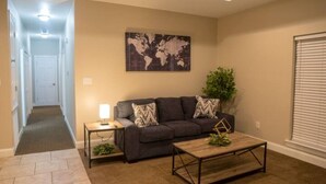 A living room with a dark-colored sofa, a coffee table, a world map on the wall, a small table with a lamp, and a plant. - Unit D (Moss Point)