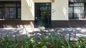A building facade with a black door, a small balcony with metal railings, and a window with a metal grill.