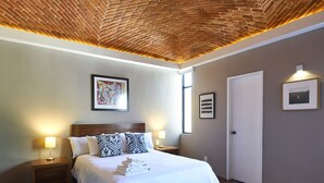 A neatly arranged hotel room with a brick ceiling, a large bed with white bedding, two bedside tables with lamps, and a framed picture on the wall.