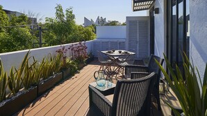 A rooftop patio with a table and chairs, surrounded by potted plants and a view of the city skyline.
