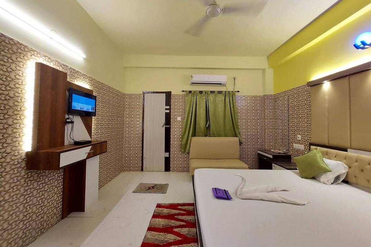 Una habitación de hotel con cama, escritorio con televisor, armario y ventilador de techo.