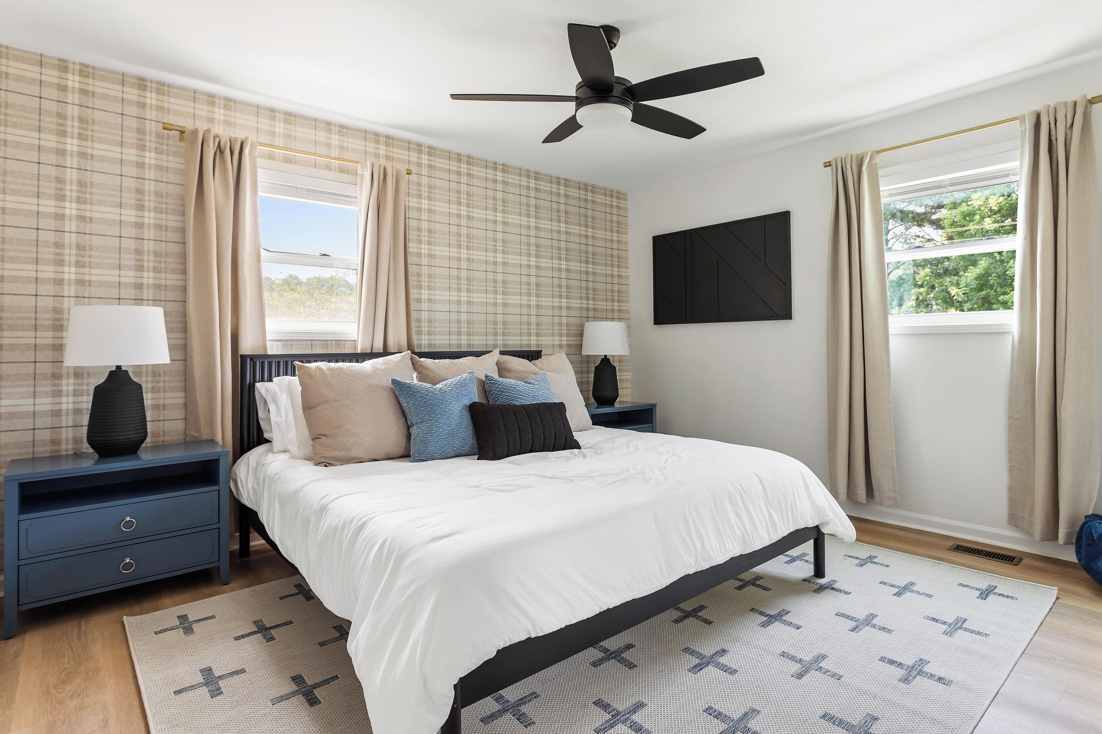 Quarto com cama, duas mesas de cabeceira, ventoinha no teto e janela com cortinas.