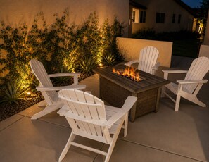 Een terras met een vuurplaats, witte Adirondack-stoelen en een tafel.