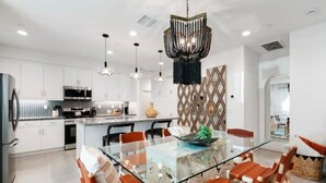 Una cocina moderna con armarios blancos, una mesa de comedor de vidrio y sillas color naranja.