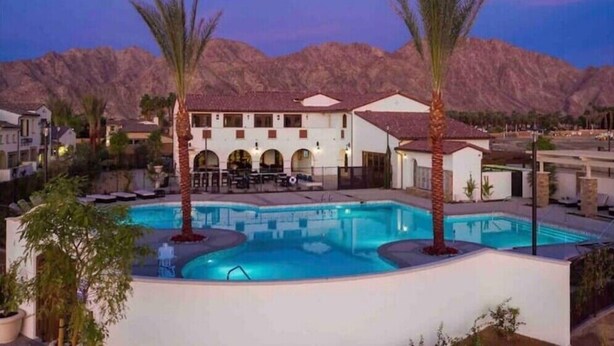 Un resort con piscina, palmeras y montañas al fondo.