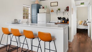 A modern kitchen with a central island, bar stools, a refrigerator, and a microwave. - Tiny Cottage - Hill Country (Kyle)