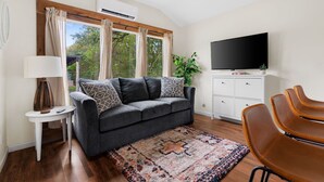 A living room with a grey sofa, a TV, a small table with a lamp, and a patterned rug. - Tiny Cottage - Hill Country (Kyle)