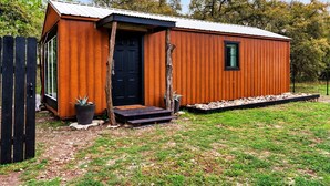 A small wooden cabin with a black door, a window, and a small porch area. - Tiny Cottage - Hill Country (Kyle)
