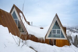 A snow-covered triangular-roofed building with a wooden exterior and large windows. - Alpine House #2  + Nordic Sauna (Steamboat Springs)