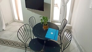 A small room with a round table, four chairs, a flat-screen TV, a potted plant, and a blue folder.