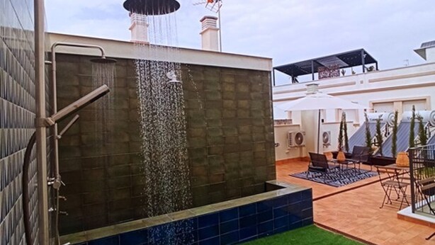 A rooftop pool with a waterfall feature, a covered seating area, and artificial grass.