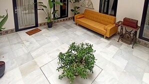 A spacious indoor area with a tiled floor, a sofa, potted plants, and a small table.